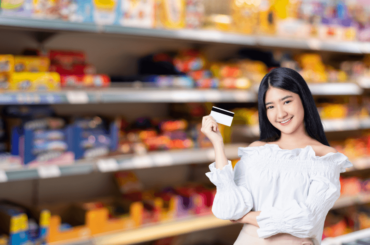 Mujer con una tarjeta frente a los pasillos de los supermercados - Tarjeta EBT
