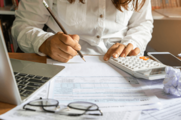 mujer trabajando en su escritorio, escribiendo notas y usando una calculadora