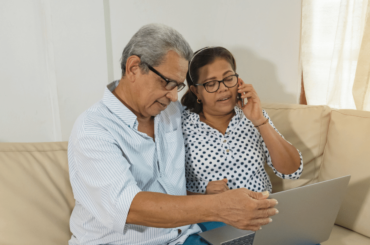 Pareja de mayores latinos que navegan por la web con una computadora portátil y un teléfono celular - Residente Permanente para Padres